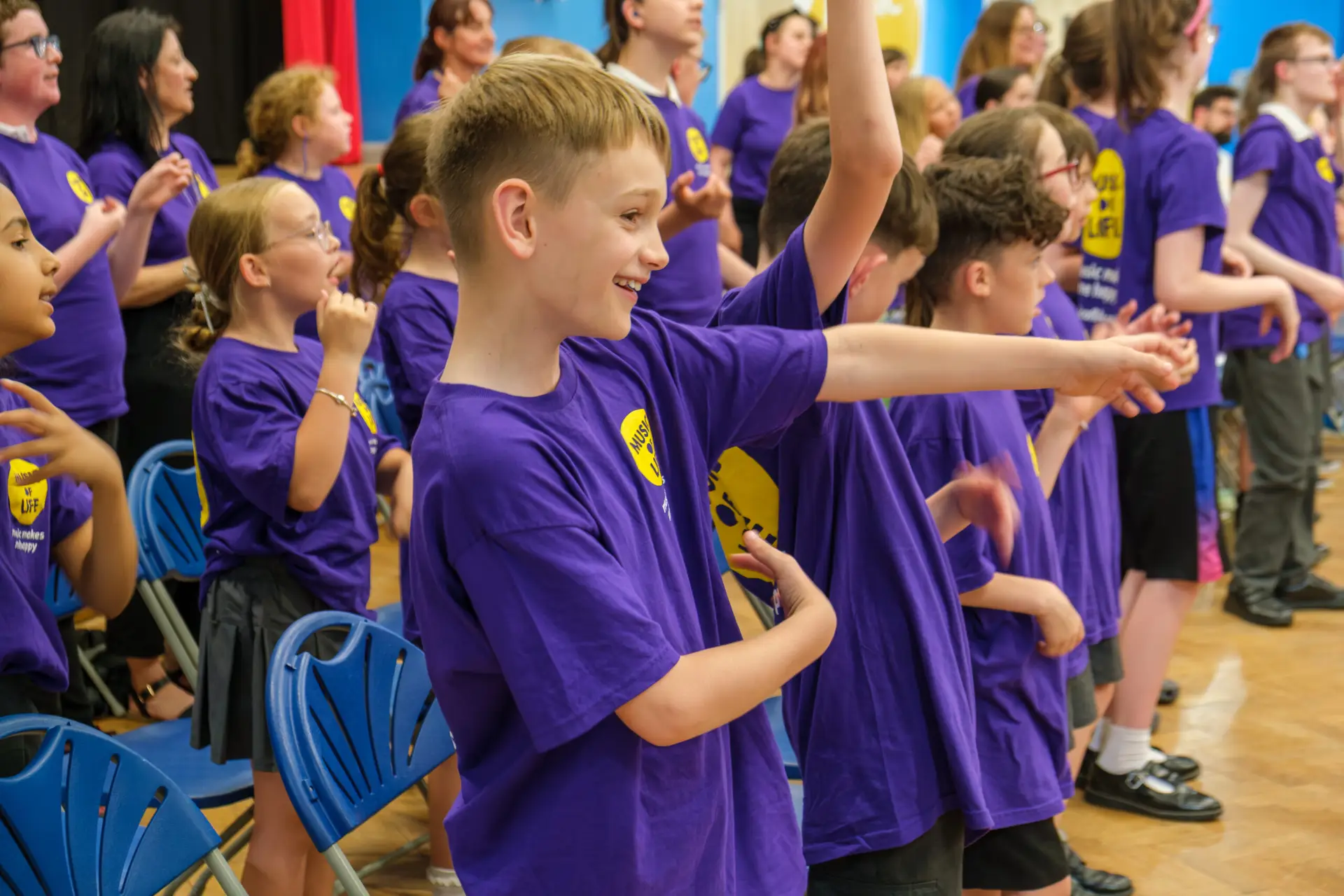 Children in purple shirts enthusiastically participating in a lively group activity at an indoor event.
